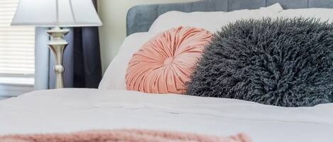 A bed with a white duvet, a peach-colored pillow, and a gray fluffy pillow.