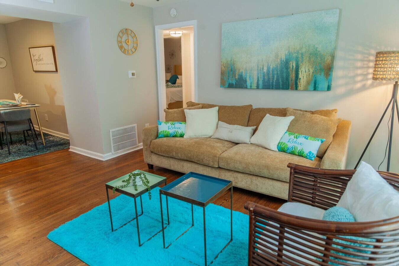 A living room with a beige sofa, two side tables, a blue rug, and a painting on the wall.