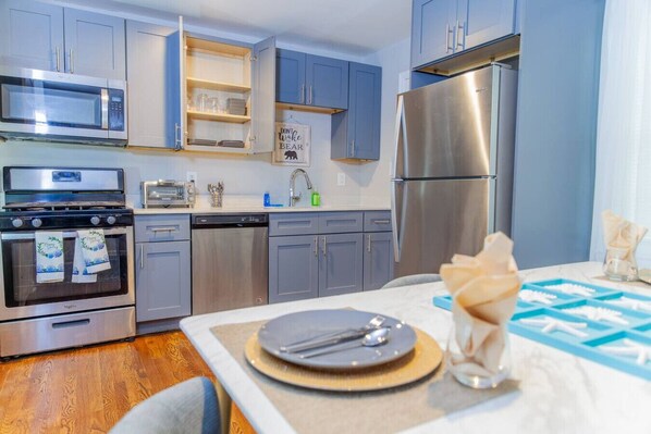 A modern kitchen with stainless steel appliances, grey cabinets, and a dining area with a table set for two. - Cozy Inside, All Things Outside (Decatur)