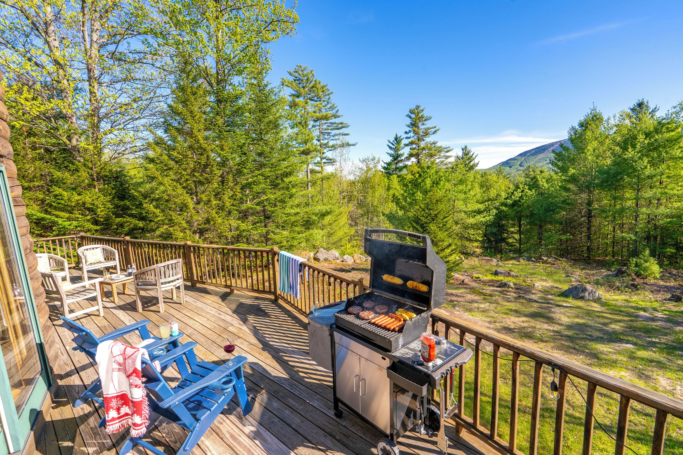 Eine Terrasse mit Grillmöglichkeit, Sitzgelegenheiten und Blick auf eine bewaldete Landschaft.