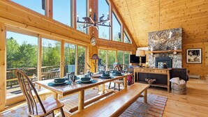 A spacious wooden cabin with large windows, a dining area, a fireplace, and a loft bed. - Relaxing Newry Chalet | Fire Pit, Hot Tub & Sauna (Newry)