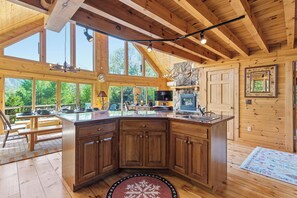 A spacious kitchen with a large island, wooden beams, and large windows offering a view of the outdoors.
