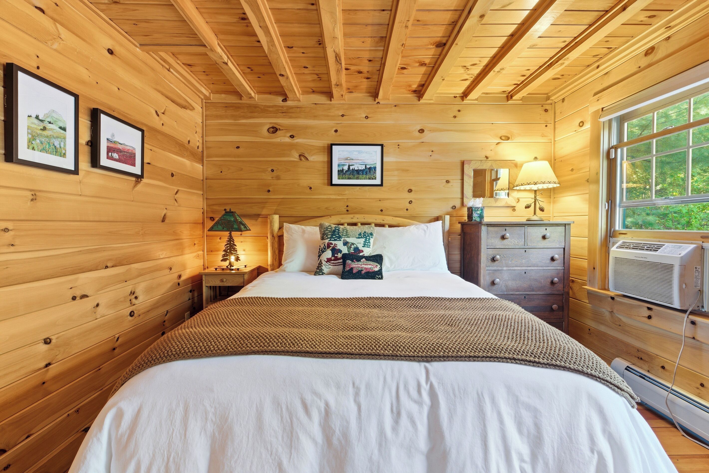 Ein Schlafzimmer mit Holzwänden, einem Bett, einer Nachttischlampe, einem Schminktisch und gerahmten Bildern an der Wand.