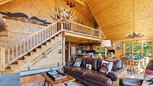 A wooden cabin interior with a staircase, a leather sofa, a dining area, and a kitchen. - Relaxing Newry Chalet | Fire Pit, Hot Tub & Sauna (Newry)