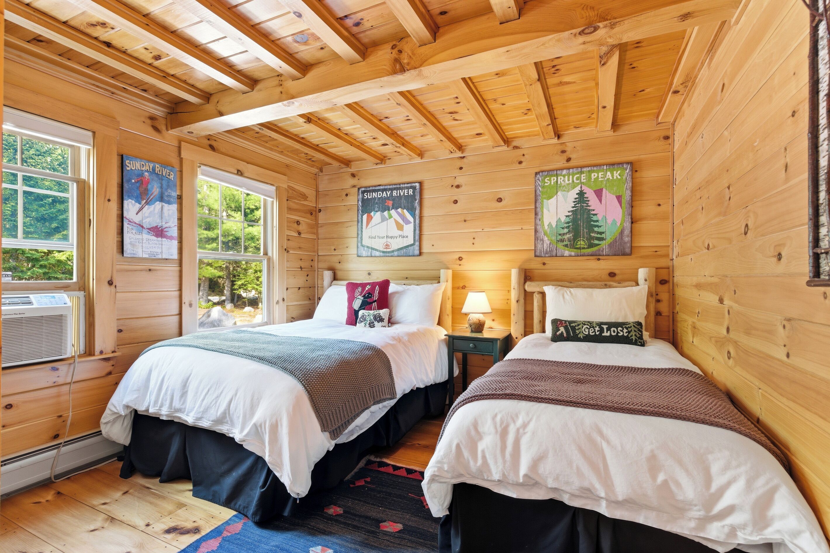 A cabin with two wooden beds, a window with an air conditioner, and posters on the walls.