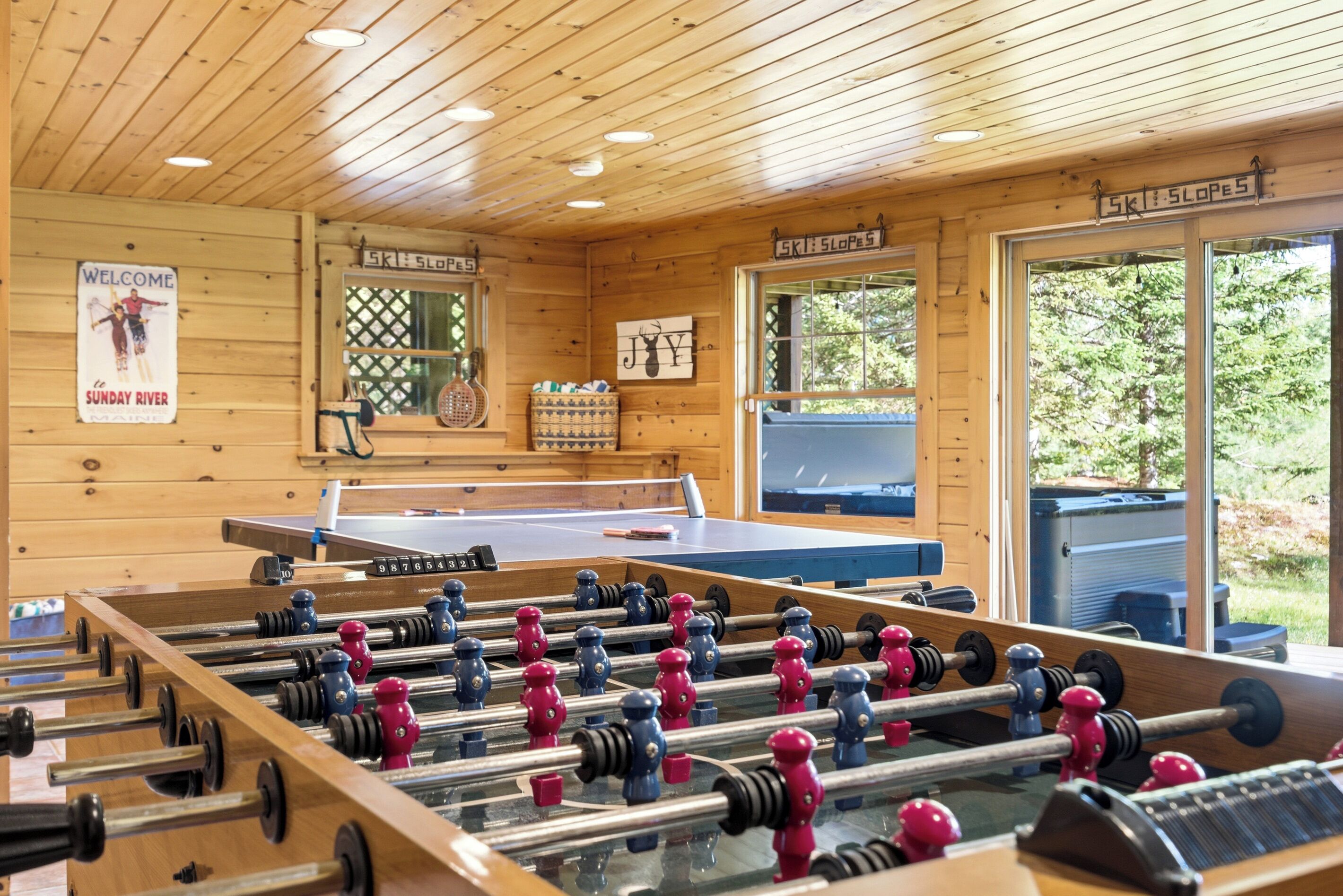 Een kamer met houten vloer, voorzien van een tafelvoetbaltafel, een pingpongtafel en een bordje met de tekst 'SKI SLOPES'.