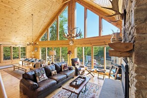 A spacious log cabin interior with a large wooden ceiling, a fireplace, a leather sofa, and a dining area.