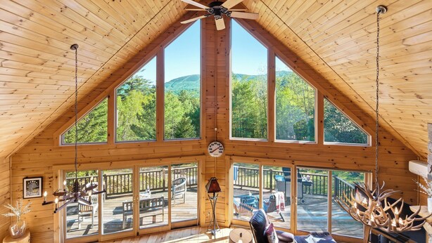 A cabin with a sloped roof, large windows, a ceiling fan, and a deck with outdoor furniture. - Relaxing Newry Chalet | Fire Pit, Hot Tub & Sauna (Newry)