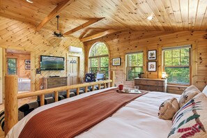 Une chambre dans un chalet en bois, avec un lit, une télévision, un bureau et une fenêtre.