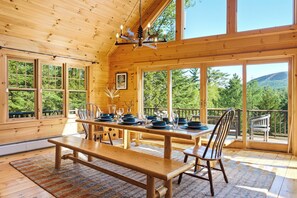 A wooden cabin with large windows, a dining table set with plates and glasses, and a bench.