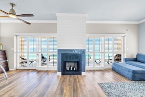 Ein Wohnzimmer mit Kamin, Holzboden, einem blauen Sofa und einem Deckenventilator.