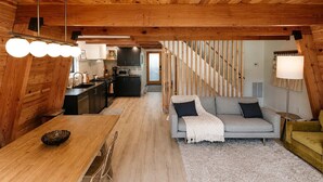 A modern interior with a wooden ceiling, a kitchen with dark cabinets, a grey sofa, and a staircase. - Modern & Cozy, Family-Friendly Cabin (Lake Arrowhead)