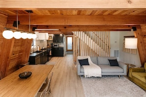 Un interior moderno con techo de madera, una cocina con armarios oscuros, un sofá gris y una escalera.