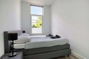 A small, modern bedroom with a bed, a bedside lamp, and a window. - Bright Apartment with Private Terrace (Rotterdam)