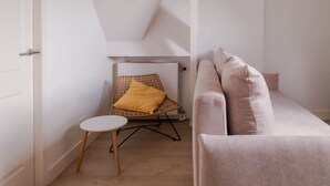 Ein modernes Schlafzimmer im Loft-Stil mit schrägem Dach, einer weißen Wand, einem beigen Sofa, einem kleinen runden Tisch und einer Pendelleuchte.