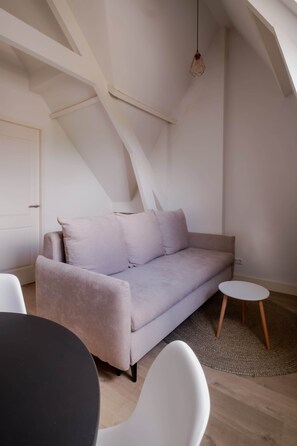 Ein modernes Schlafzimmer im Loft-Stil mit hohen Decken, freiliegenden Balken, einem hellen Sofa, einem runden Tisch und einer hängenden Leuchte.