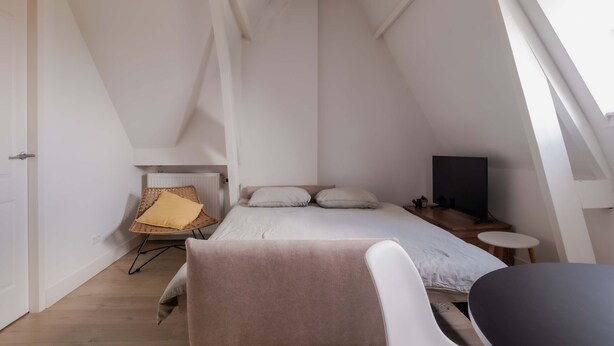 Ein Schlafzimmer mit einem Bett, einem Sessel, einem Fernseher und einem kleinen Tisch.