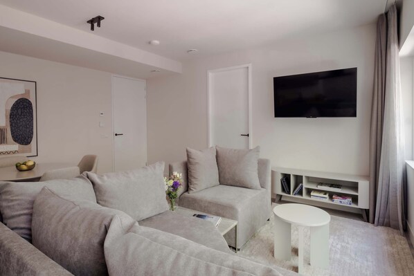 Een moderne woonkamer met een modulaire bank, een salontafel, een flatscreen televisie aan de muur en een boekenplank.
