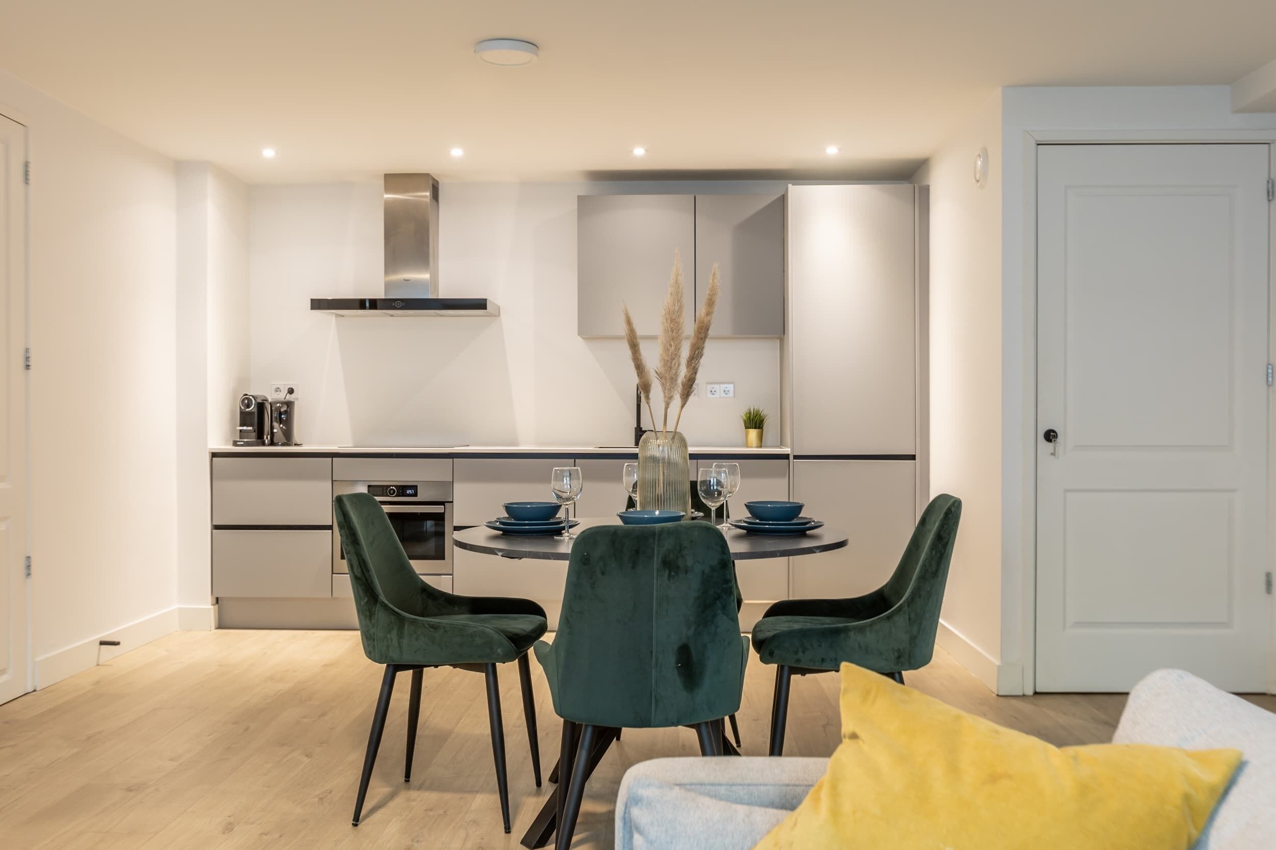 A modern kitchen with a dining area, including a round table with chairs and a vase of dried plants.