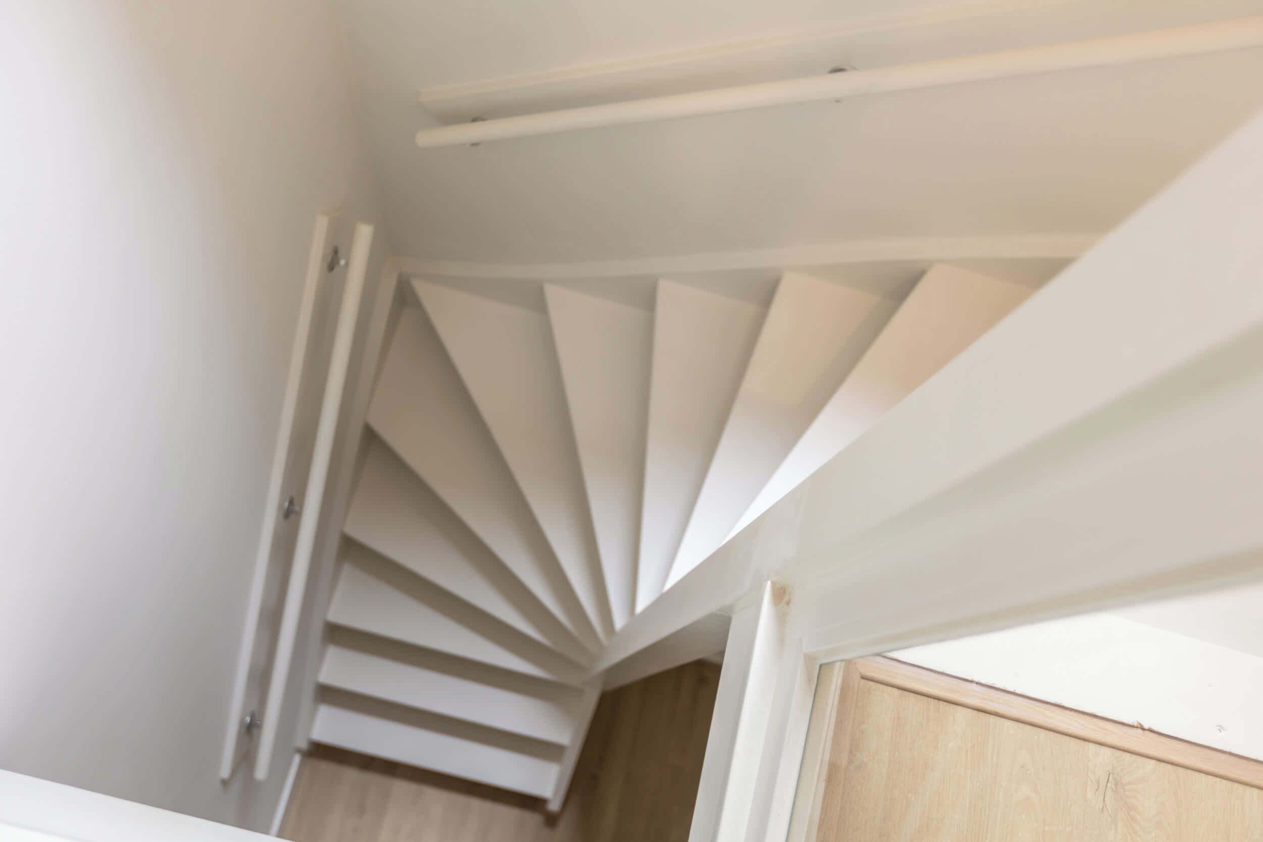 Un escalier en colimaçon blanc se trouve dans une pièce dont le sol est en bois et les murs sont blancs.