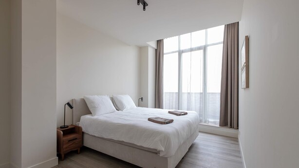 A bedroom with a bed, a nightstand, a lamp, and a window with curtains. - Modern 3BR Apartment in Rotterdam Centre (Rotterdam)