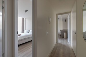 Un couloir menant à une chambre comprenant un lit, une petite kitchenette et une salle de bain.