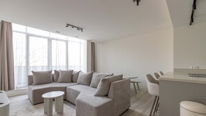 A modern living room with a sectional sofa, a small round table, and a kitchen area with bar stools. - Modern 3BR Apartment in Rotterdam Centre (Rotterdam)
