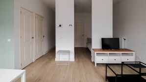Quarto moderno e minimalista com piso de madeira, mobiliário branco, uma TV sobre suporte de madeira e uma porta branca.