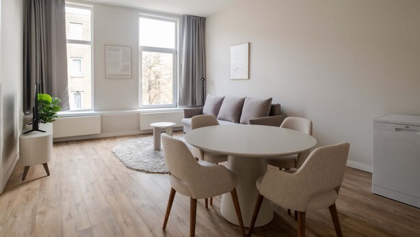 Un salón moderno con una mesa de comedor redonda, sofás beige y un radiador blanco.