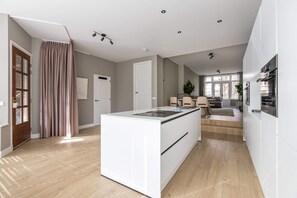 Eine moderne Küche mit einer zentralen Kochinsel, einem Essbereich mit einer Couch und einem großen Fenster, das für natürliches Licht sorgt.