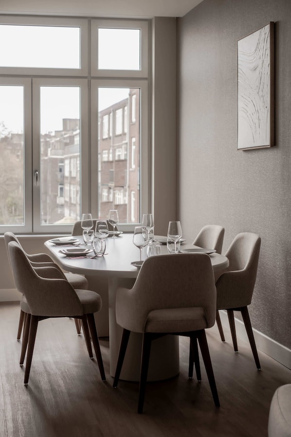 Un coin repas avec une table dressée pour six personnes, six chaises et une grande fenêtre donnant sur la ville.