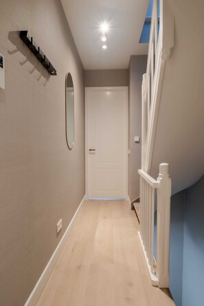 Un couloir avec un plancher en bois, une porte blanche et une rambarde blanche.