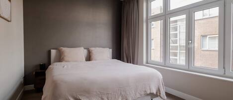 A bedroom with a large window, a bed, and a nightstand.