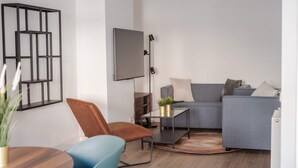 Ein modernes Wohnzimmer mit einem grauen Sofa, einem Holztisch, einem blauen Sessel und einer schwarzen Stehlampe.