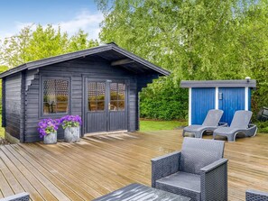 Eine Holzhütte mit einer Veranda, zwei Türen und einem kleinen Schuppen mit Stühlen.