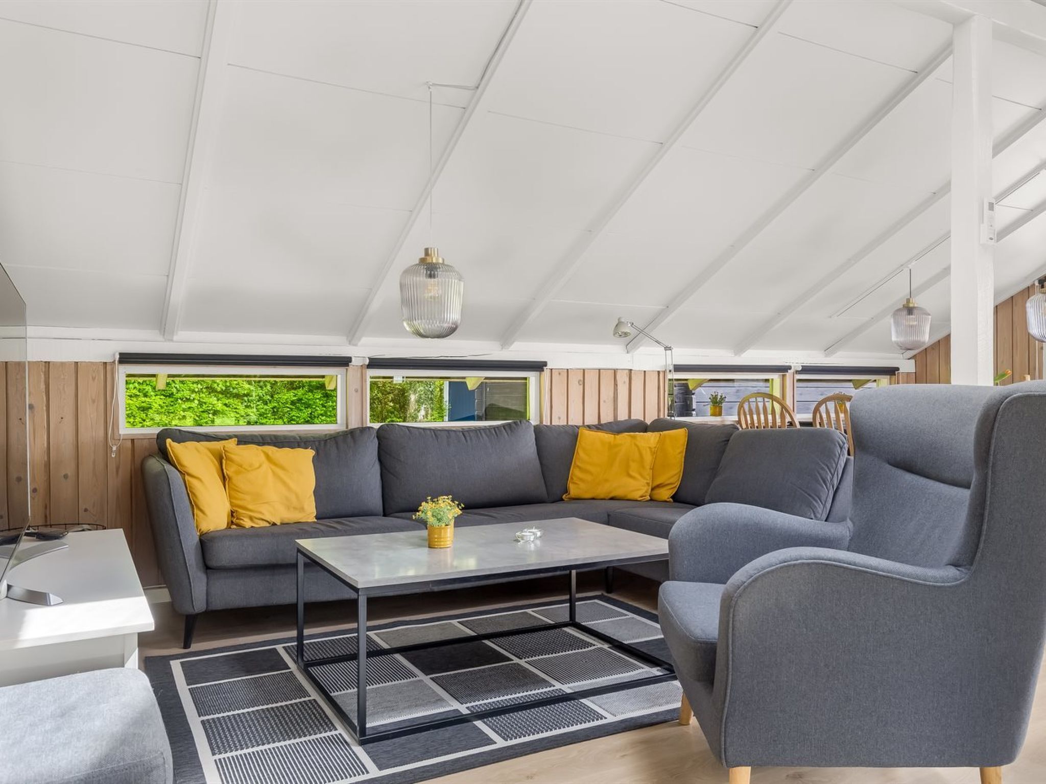 A modern living area with a sofa, armchair, and coffee table, featuring a view through large windows.