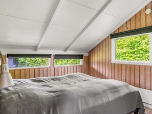 Ein Schlafzimmer mit Bett, Holzwänden, einem Fenster und einem Deckenventilator.