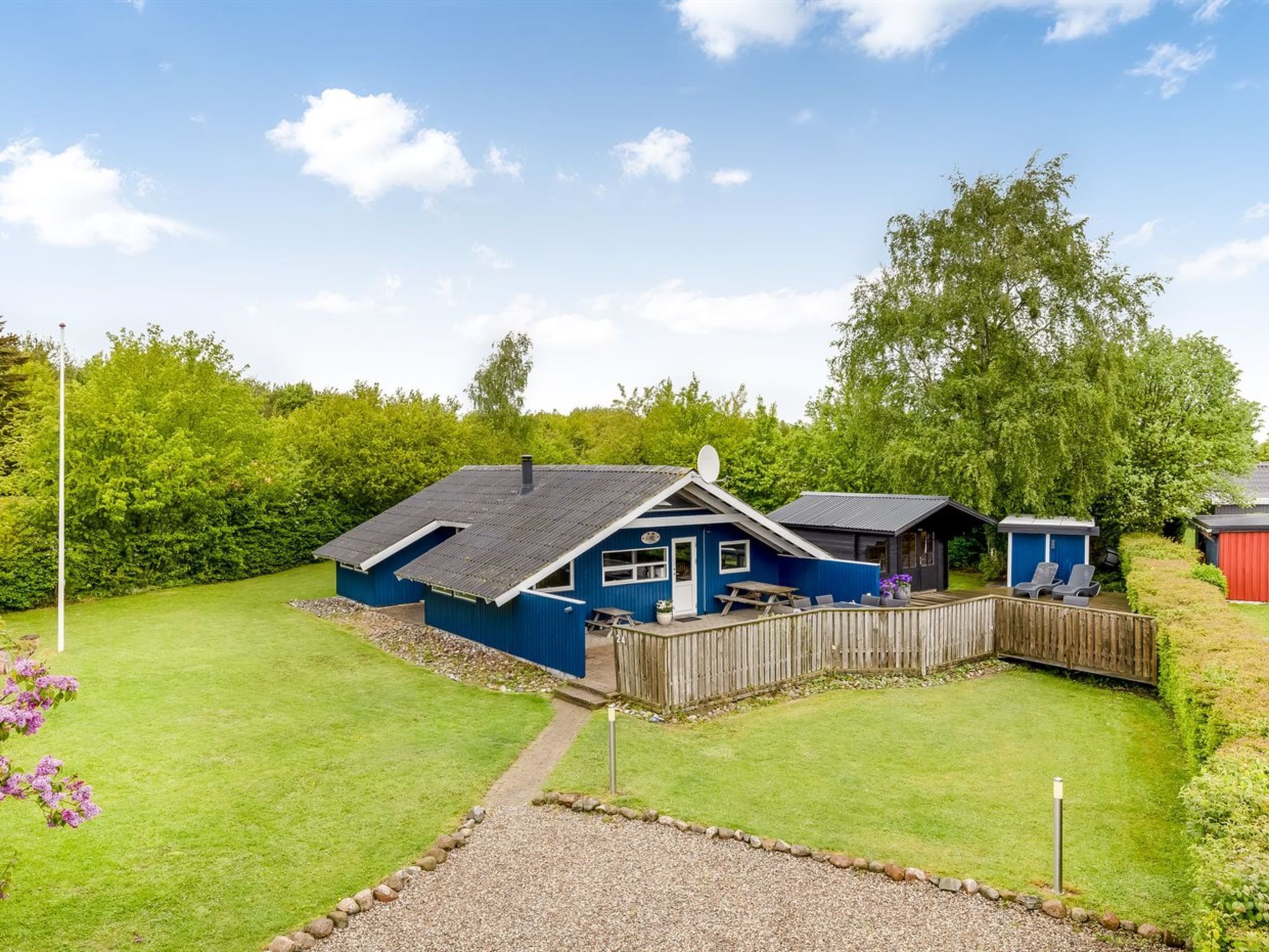A blue house with a fenced yard, a picnic table, and a red shed.