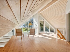 Ein Schlafzimmer im Dachgeschoss mit Holzdielen, großen Fenstern und Blick auf Grünflächen.