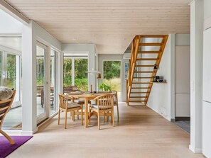 A modern interior with a wooden dining table and chairs, a staircase, and large windows. - "Aman" - 100m from the sea by Interhome (Læsø)
