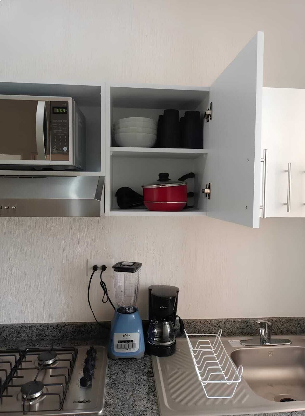 A kitchen with a microwave, a red pot, a blender, and a coffee maker.