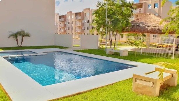 Une piscine rectangulaire bordée de blanc, entourée d’une pelouse verte et de quelques arbres.