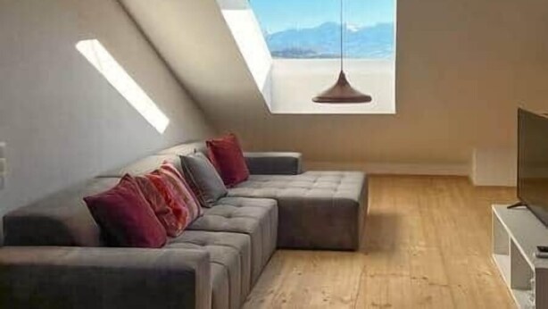 A modern loft bedroom with a large window, a sectional sofa, and a hanging light fixture.
