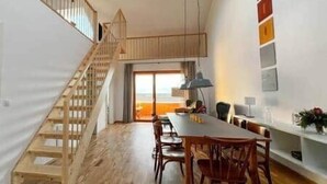 A staircase leading to a loft bedroom, a dining area with a table and chairs, and a kitchen area with a window.