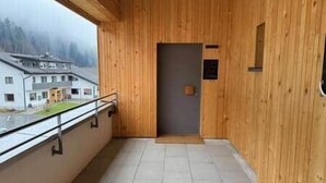 A wooden interior with a balcony, a door, and a view of buildings outside.