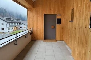 A wooden interior with a balcony, a door, and a view of buildings outside.