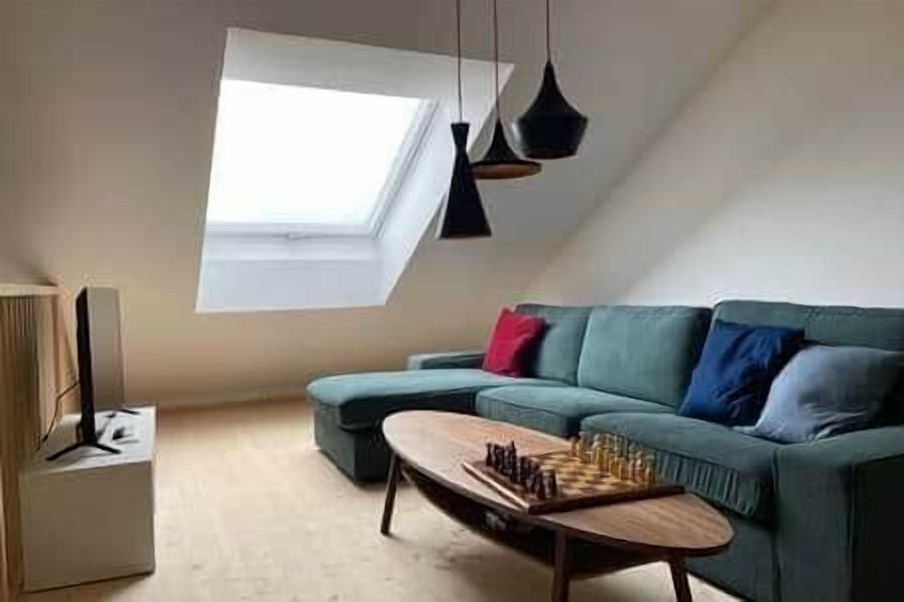 A loft-style room with a sloped ceiling, a green sofa, a wooden coffee table, and a skylight.