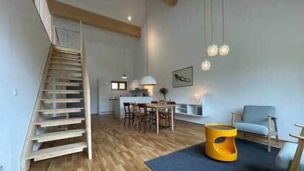 A spacious living area with a wooden staircase, a dining table, and a sofa.
