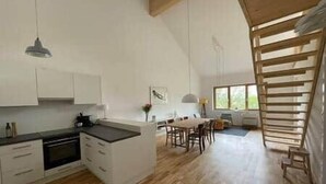 A modern kitchen with white cabinetry, a dining area with a wooden table, and a large window providing natural light.