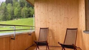 A balcony with two wooden chairs, a wooden floor, and a view of a green landscape.
